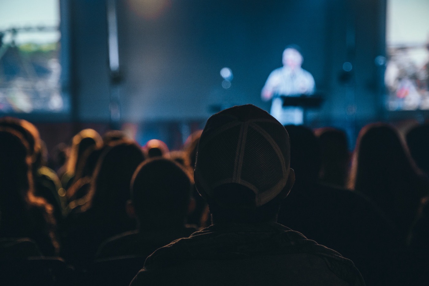 Silhouetted audience watching a backlit speaker present on stage at a conference